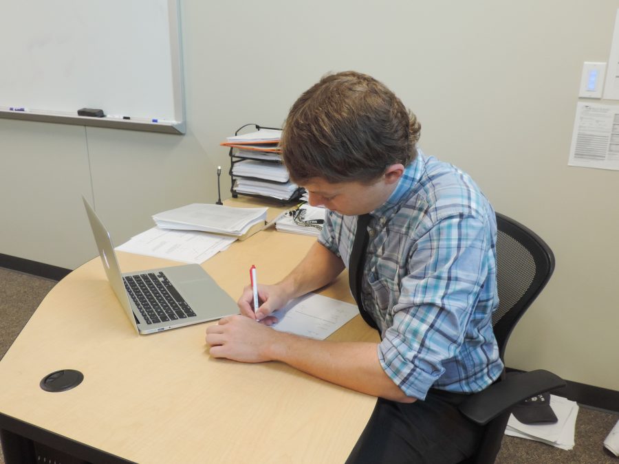 Math teacher Ian Hempe sitting down grading students papers. 
