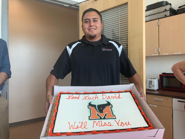 Campus supervisor David Morales poses with his going away cake, accurately scripted with 